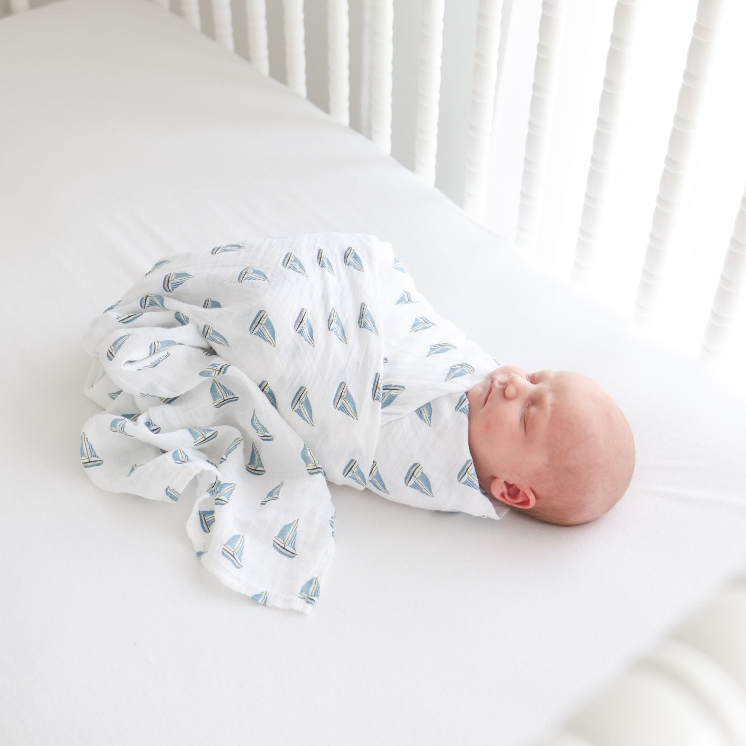 Newborn baby swaddled in a blanket with sailboat pattern in a crib.