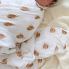 Baby swaddled in a white blanket with highland cow animal prints on a soft beige surface.
